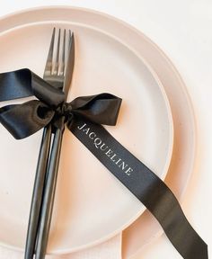 a white plate topped with a black ribbon and two silver forkes next to each other