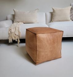 a tan leather ottoman sits in front of a white couch with throw pillows on it