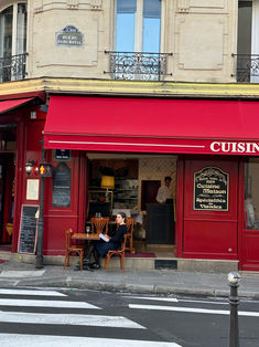 two people sitting at a table in front of a restaurant on the corner of a street