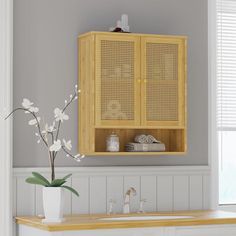 a wooden cabinet above a sink in a room with white walls and flooring, along with flowers