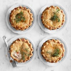 four small pies on white plates with silverware next to each other and a fork