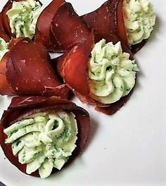 several pieces of bacon wrapped in green sauce on a white plate with a knife and fork