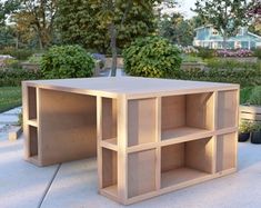 a wooden table sitting on top of a cement ground next to some bushes and trees