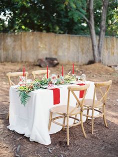 a table set up with red candles and greenery