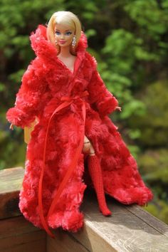 a barbie doll wearing a red fur coat on a wooden ledge with trees in the background