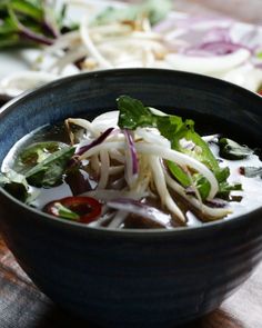 a bowl filled with soup and vegetables on top of a wooden table next to other food items