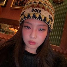 a girl with long hair wearing a knitted hat and looking at the camera while standing in front of a clock