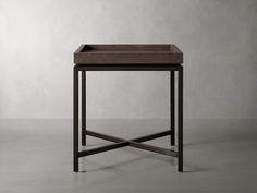 a square wooden table with a metal base and brown leather tray on the top, in front of a gray wall