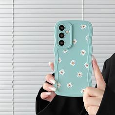 a woman holding up a phone case with daisies on it