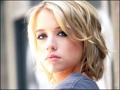 a woman with blonde hair and blue eyes looks into the distance while standing in front of a building