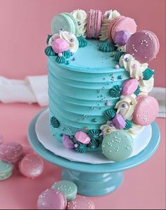 there is a blue cake with pink and green decorations on the top, next to some cookies