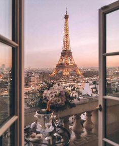 the eiffel tower is lit up at night from an open window with flowers