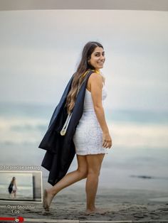 a woman is walking on the beach with her coat over her shoulders