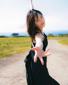 a woman in black dress standing on dirt road with her arms out and hands outstretched