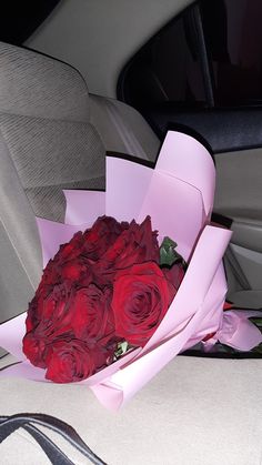 a bouquet of red roses is sitting in the back seat of a car, wrapped in pink paper