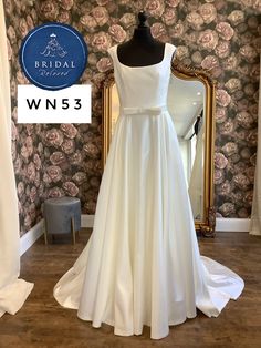 a white wedding dress is on display in front of a floral wallpapered room