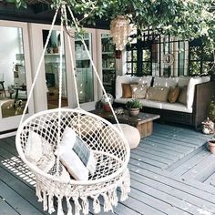 a white hanging chair sitting on top of a wooden floor next to a patio area