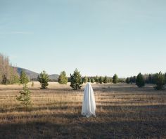 a woman in a long white dress standing in a field