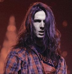 a man with long hair wearing a plaid shirt and holding a guitar in his hands