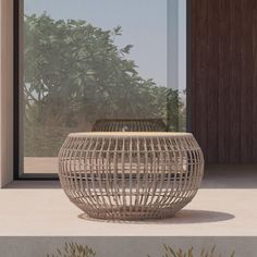 a round wicker table sitting on top of a cement floor next to a window