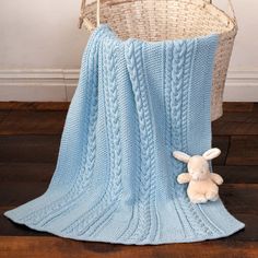 a knitted blanket with a stuffed bunny on the floor next to it and a basket