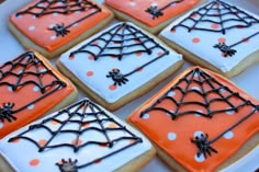 halloween cookies decorated with icing and spider webs are on a white platter