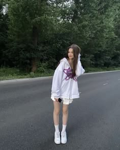 a woman standing on the side of a road wearing a white hoodie and shorts