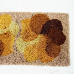 a brown and yellow rug with flowers on it's side in front of a white wall