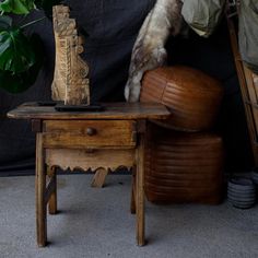 a wooden table topped with a vase next to a brown chair and potted plant