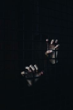 a person holding their hands out through the bars of a caged in area that is dark