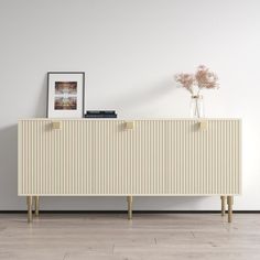 a white and gold sideboard with vases on it next to a painting, lamp and flowers