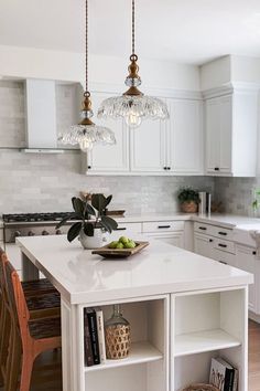 a white kitchen with an island in the middle and two pendant lights hanging from the ceiling