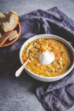 a white bowl filled with soup next to a basket of bread and a spoon on a blue cloth