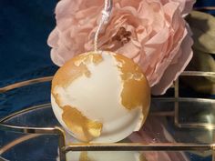 a white and gold globe ornament sitting on top of a glass plate next to a pink flower