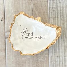 the word is your oyster on a white and gold shell with black lettering that reads, the world is your oyster