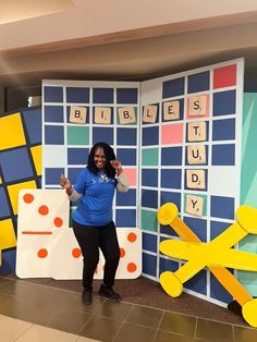 a woman standing in front of a wall with blocks and letters on it, giving the thumbs up