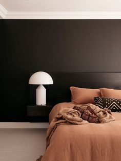 a bedroom with black walls and brown linens on the bed, along with a white floor lamp