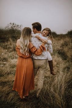 a man and woman are walking through the grass with their arms around each other as they hug