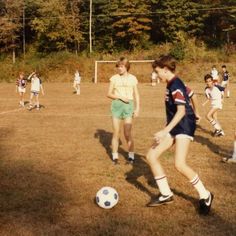 young children playing soccer on a field with trees in the backgroung area