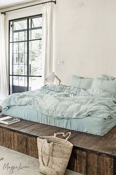 a large bed sitting under a window next to a wooden table with a basket on it