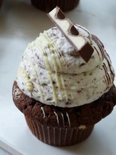 a chocolate cupcake topped with whipped cream and chocolate pieces on top, sitting on a white surface