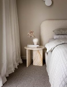 a white bed sitting next to a table with a vase filled with flowers on top of it