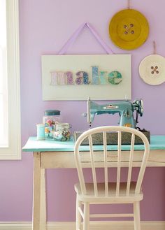 a sewing machine sitting on top of a wooden table next to a white chair in front of a purple wall