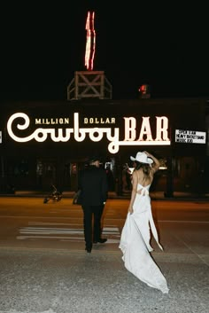 a bride and groom walking in front of the neon sign for the million dollar cowboy bar