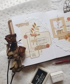 a close up of a book with flowers and some writing implements on it next to a stamp pad