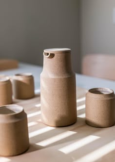 three vases sitting on top of a wooden table next to cups and containers with lids