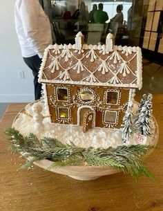 a gingerbread house with icing and decorations on a wooden table in front of a man