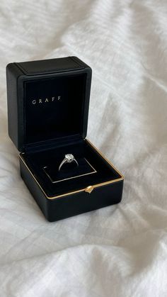 an open black box with a ring inside on a white bed sheet that says craft