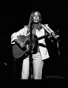 a black and white photo of a woman singing into a microphone while holding a guitar