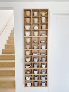 a wooden shelf filled with cups and saucers next to a stair case on the wall